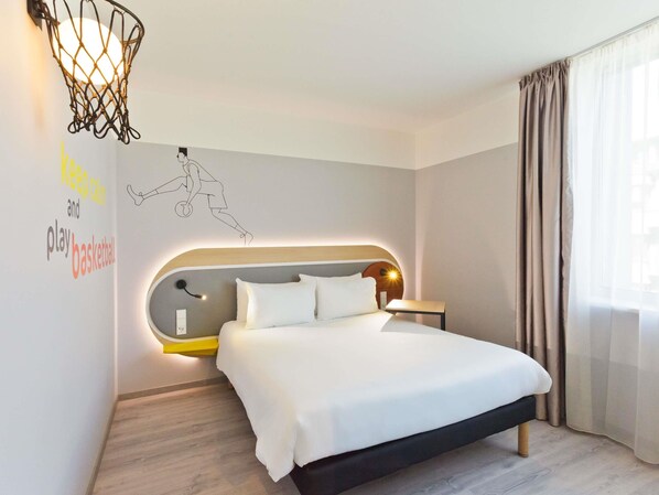 A modern hotel room with a bed, a wall-mounted basketball player illustration, and a basketball hoop light fixture. - Ibis Styles Kaunas Centre (Kaunas)