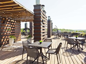 An outdoor patio with wooden decking, metal chairs, and tables. - Ibis Styles Kaunas Centre (Kaunas)