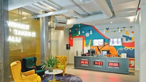 Zona de recepción de un hotel con decoración colorida, un mostrador de recepción que muestra información de los huéspedes y arreglos de asientos.