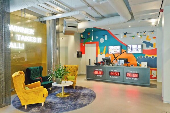 Zona de recepción de un hotel con decoración colorida, un mostrador de recepción que muestra información de los huéspedes y arreglos de asientos.