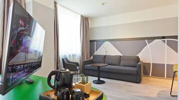 Una habitación de hotel moderna con televisión de pantalla plana, un sofá, una mesita y una bandeja con teteras.