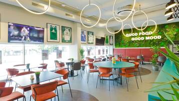 A restaurant with round tables, orange chairs, and a green wall with a 'GOOD FOOD GOOD MOOD' sign.