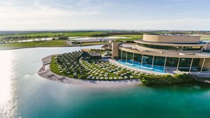 Vista aérea de un resort con un área de piscina circular, un edificio grande con techo curvo y un paisaje circundante.