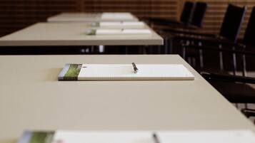 Een vergaderzaal met lange tafels, elk voorzien van een notitieblok en pen.