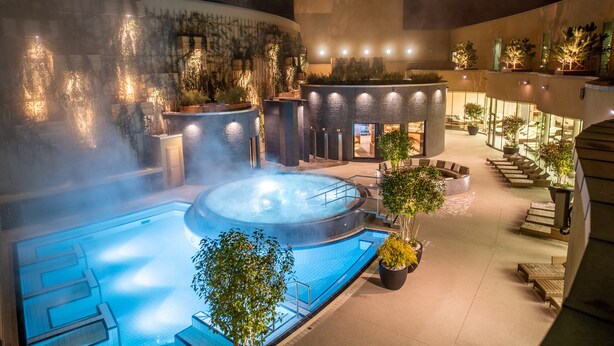 Zona de piscina exterior climatizada con asientos y plantas.