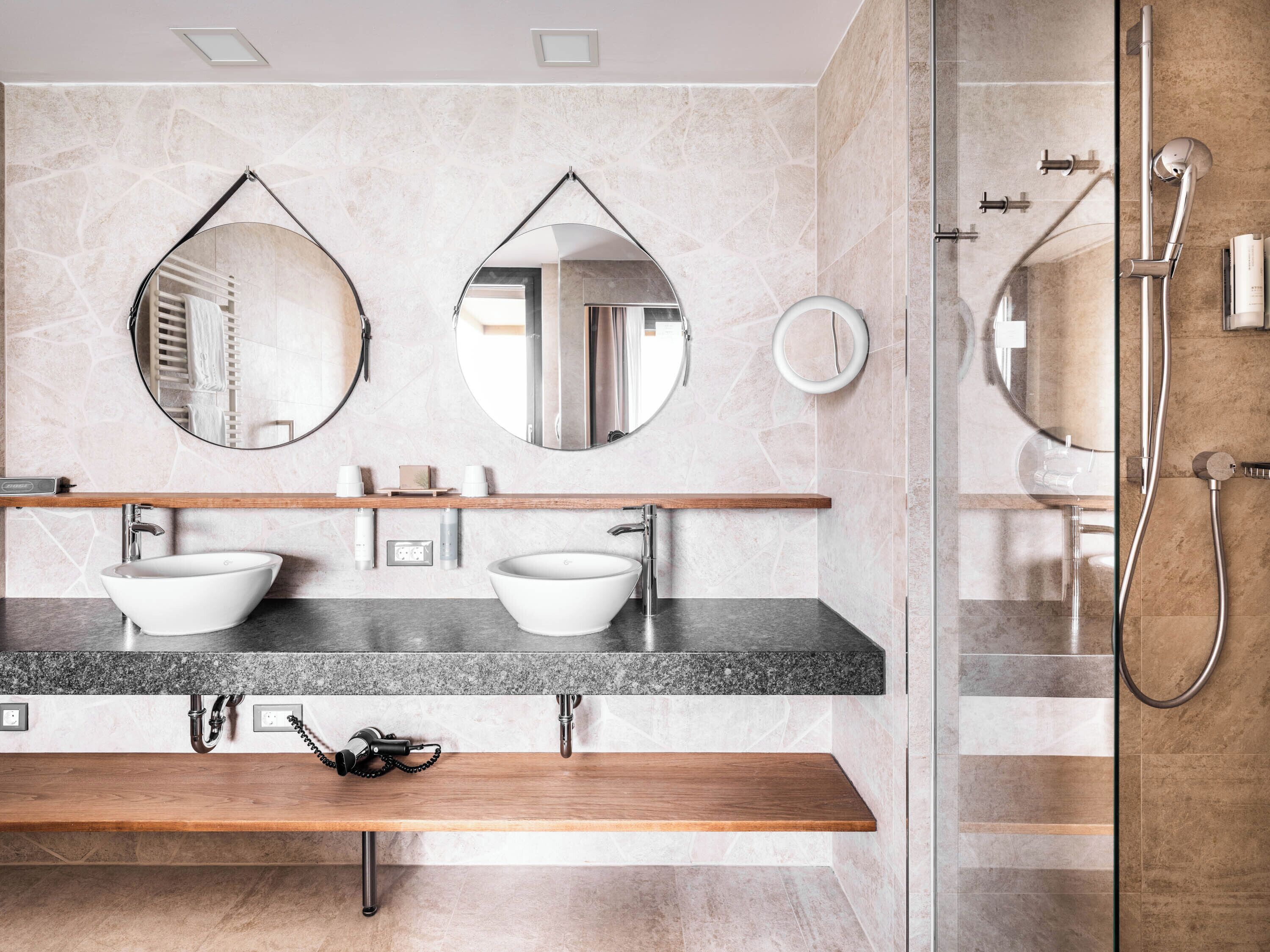 A modern bathroom with two vessel sinks, a wooden vanity, and a glass-enclosed shower area.