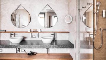 Un baño moderno con dos lavamanos sobre encimera, un mueble de tocador de madera y una zona de ducha con mampara de vidrio.