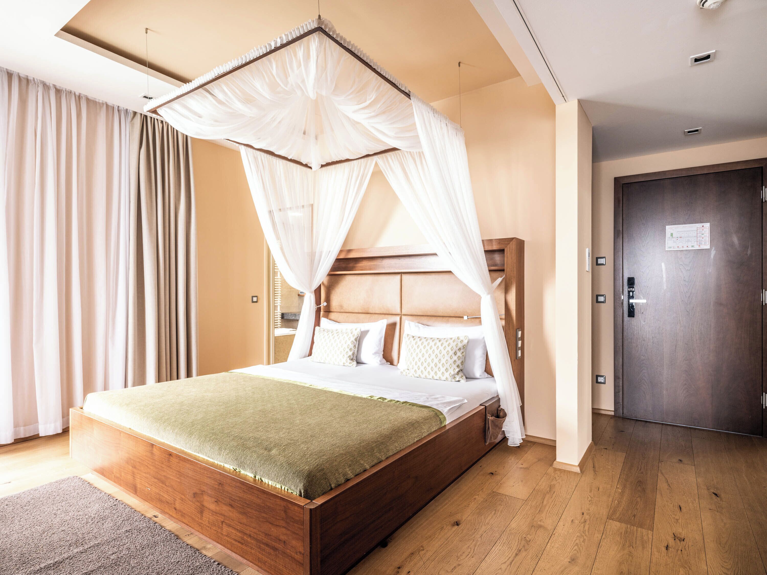 A bedroom with a wooden bed, a canopy, a wooden door, and a view of the hallway.