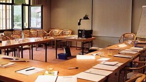 Una sala de conferencias con mesas largas, sillas, una pantalla de proyector y una pizarra.
