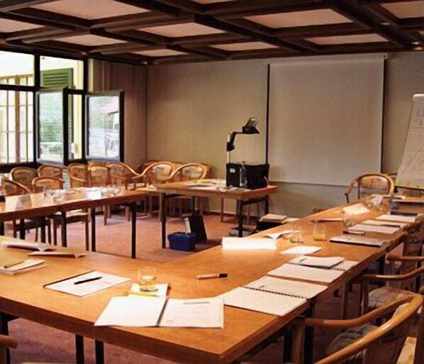 A conference room with long tables, chairs, a projector screen, and a whiteboard.