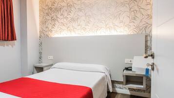 A hotel room with a bed, a nightstand, a desk with a lamp, and a wall with a bamboo pattern.