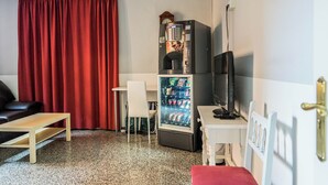 Een compacte kamer met een bank, een tafeltje, een koelkast vol drankjes en een televisie.