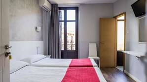 Een hotelkamer met twee bedden, een raam met gordijnen, een deur, een aan de muur bevestigde televisie en een klein tafeltje.