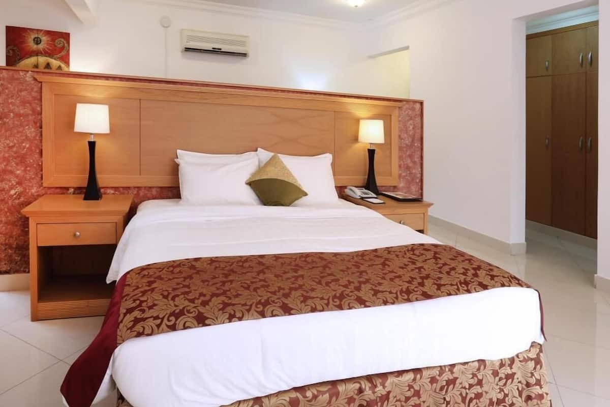 A hotel room with a large bed, two bedside tables with lamps, a wooden headboard, a telephone, and a wardrobe.