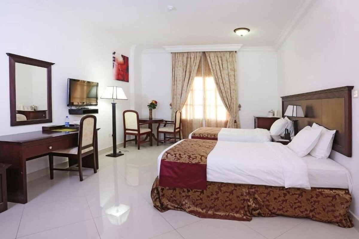 A hotel room with a bed, a desk, a chair, a TV, and a window with curtains.