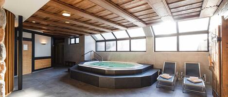 A spa area with a hot tub, two lounge chairs, and a stone wall.