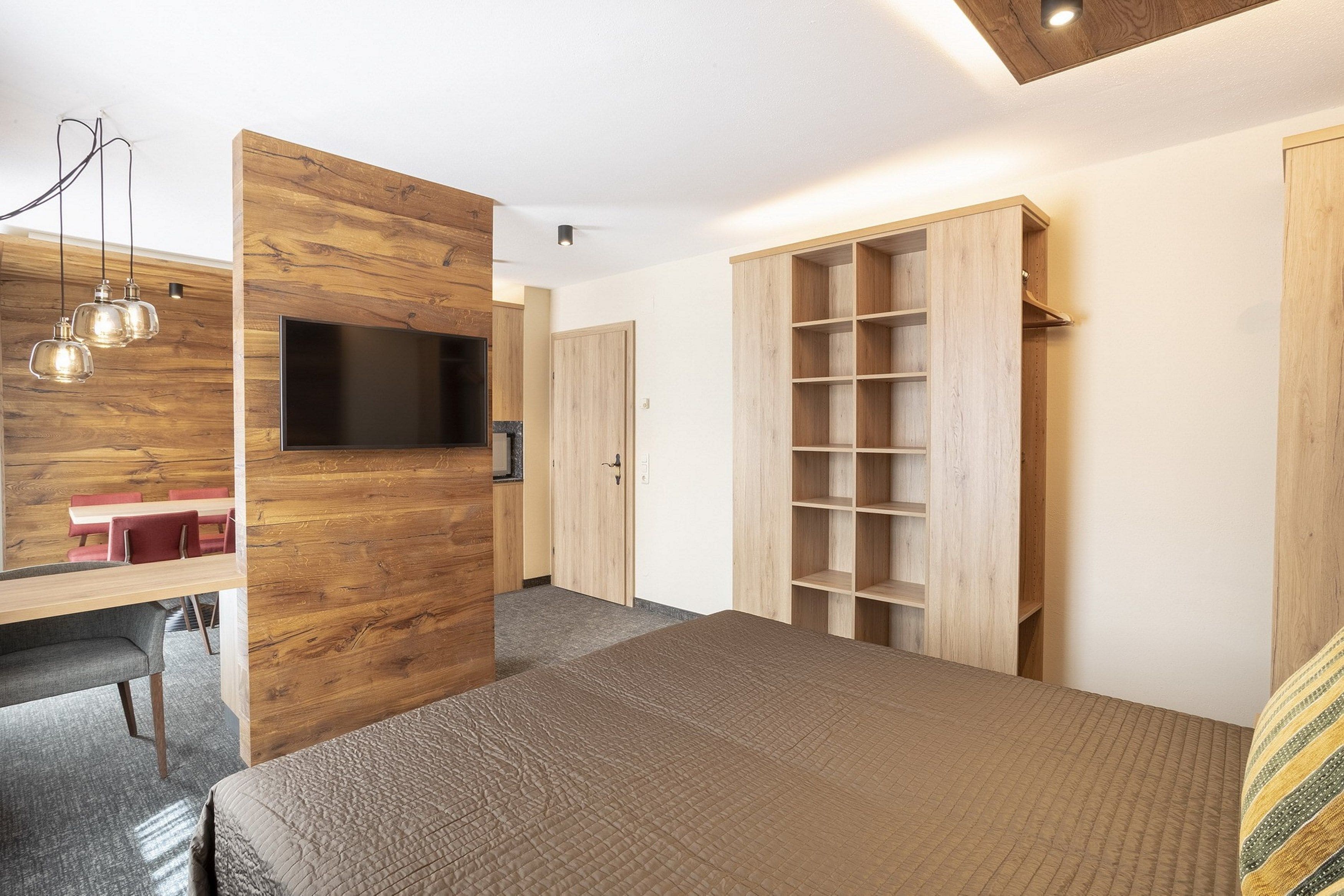 A modern bedroom with a wooden wall, a bed, a TV, and a wardrobe.