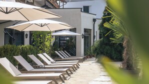 A row of sun loungers with umbrellas, a modern building, and potted plants.
