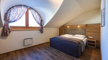A bedroom with a sloped ceiling, a bed with a headboard, a window with curtains, and a wall-mounted heater.