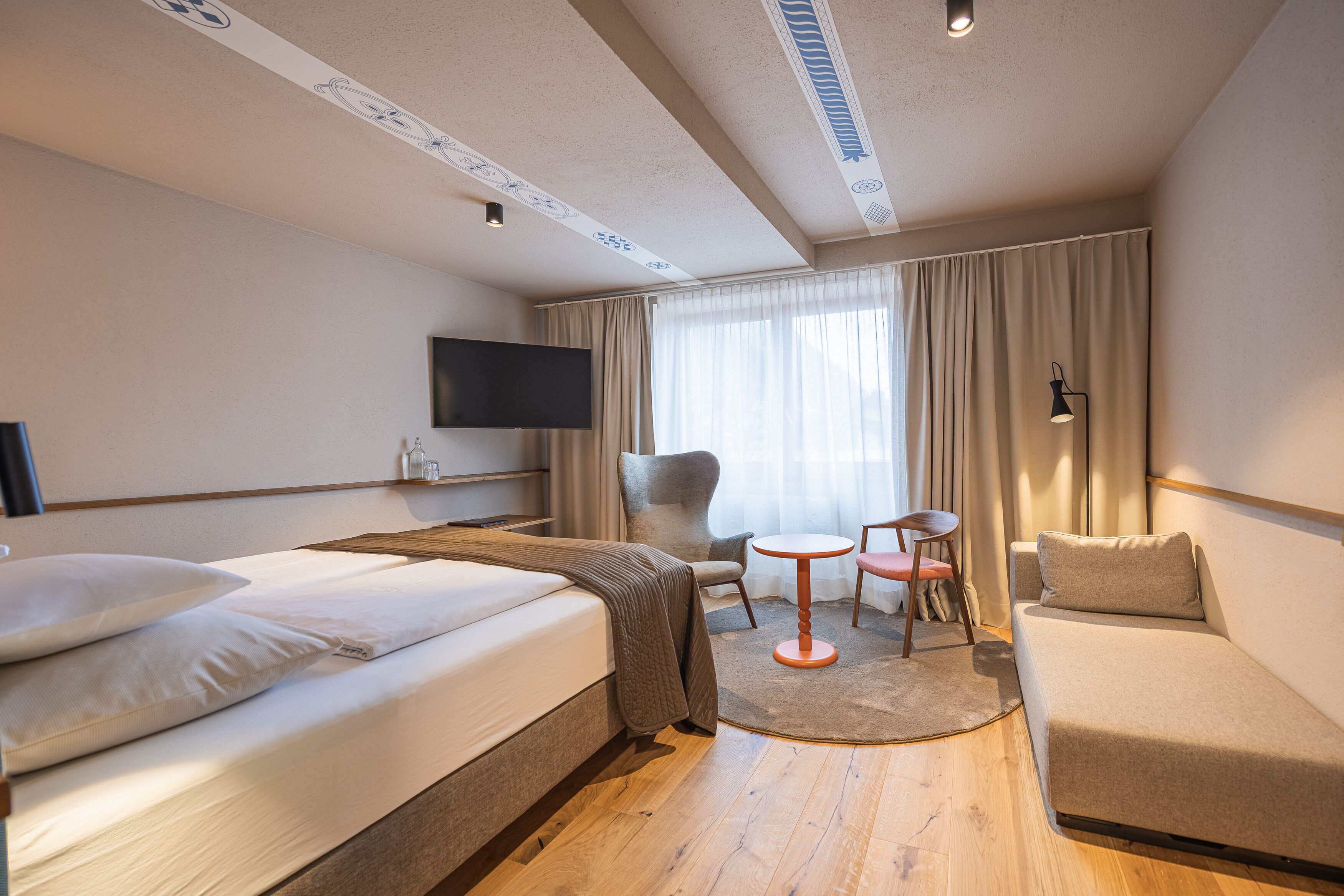 A hotel room with a bed, a sofa, a small table, a chair, a TV, and a window with curtains.