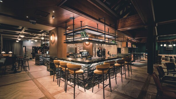 A bar area with a marble counter, bar stools, and a high ceiling with exposed beams.