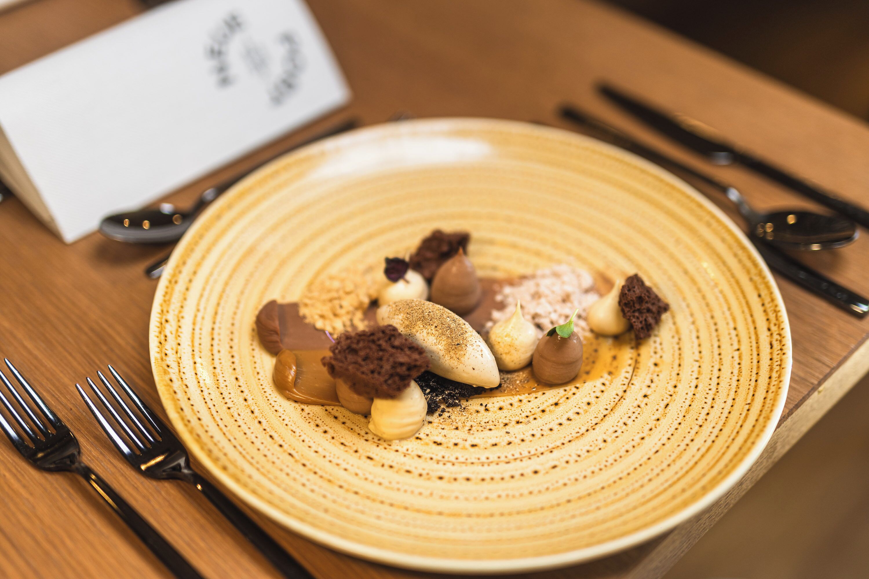 A plate of dessert with various toppings, accompanied by a fork and spoon on a wooden table.