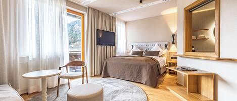 A hotel room with a bed, a desk, a chair, a round ottoman, a TV, and a large mirror.