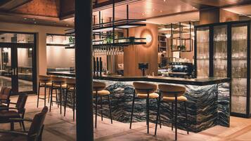 Un espace bar moderne doté d’un comptoir en marbre, de tabourets de bar et d’un grand miroir.