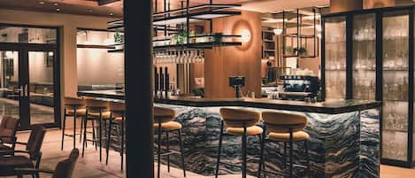 Un espace bar moderne doté d’un comptoir en marbre, de tabourets de bar et d’un grand miroir.