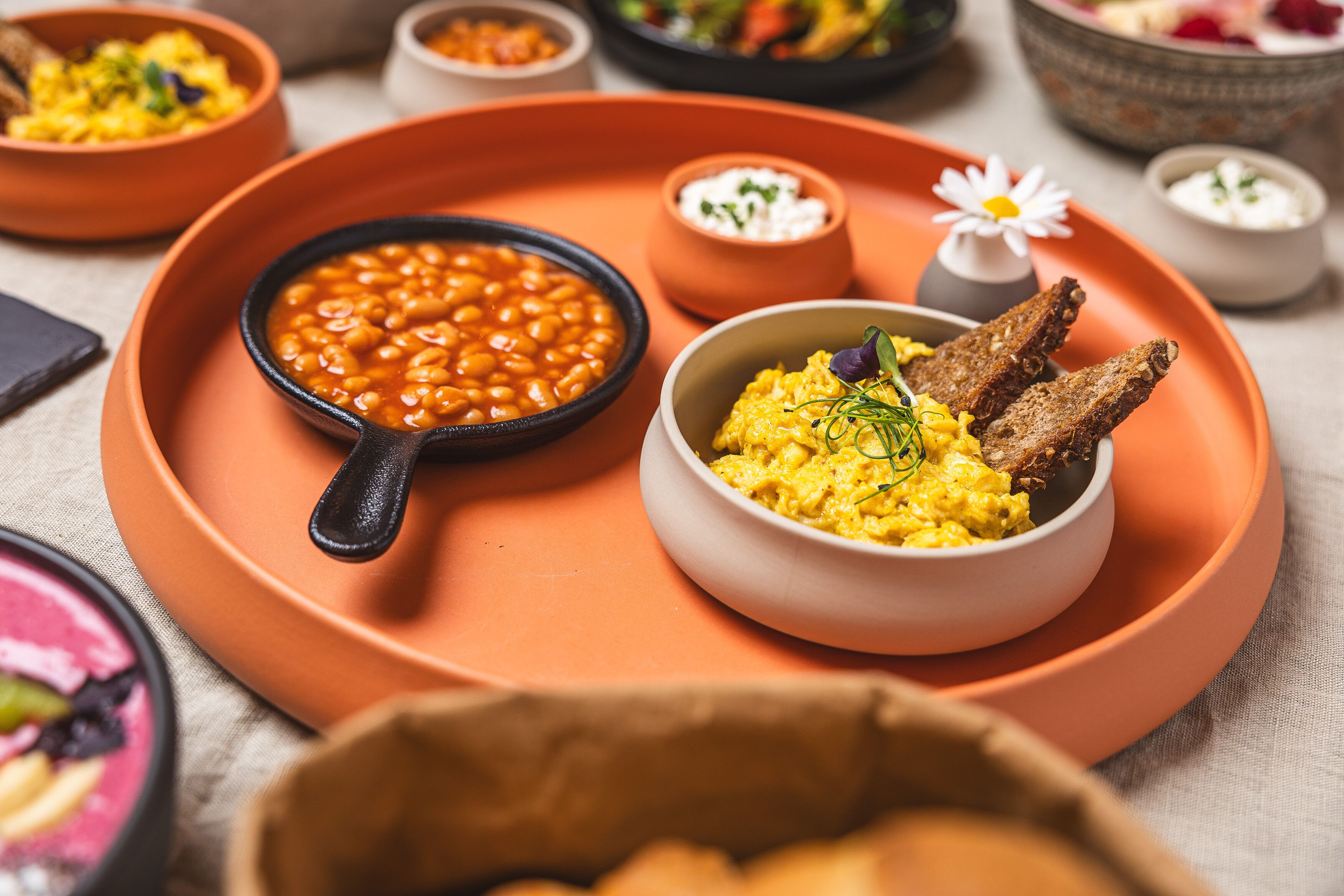 Un plateau de petit-déjeuner avec une poêle de haricots, un bol d’œufs brouillés et des tranches de pain grillé.