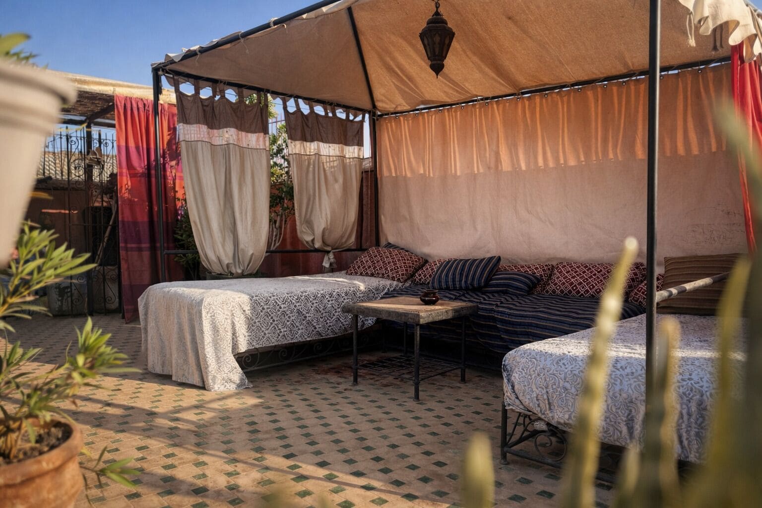 A cozy outdoor seating area with two cushioned benches, a small table, and a canopy providing shade.