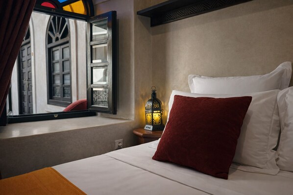 A hotel room with a bed, a nightstand with a lantern, and a window with a view of a building.