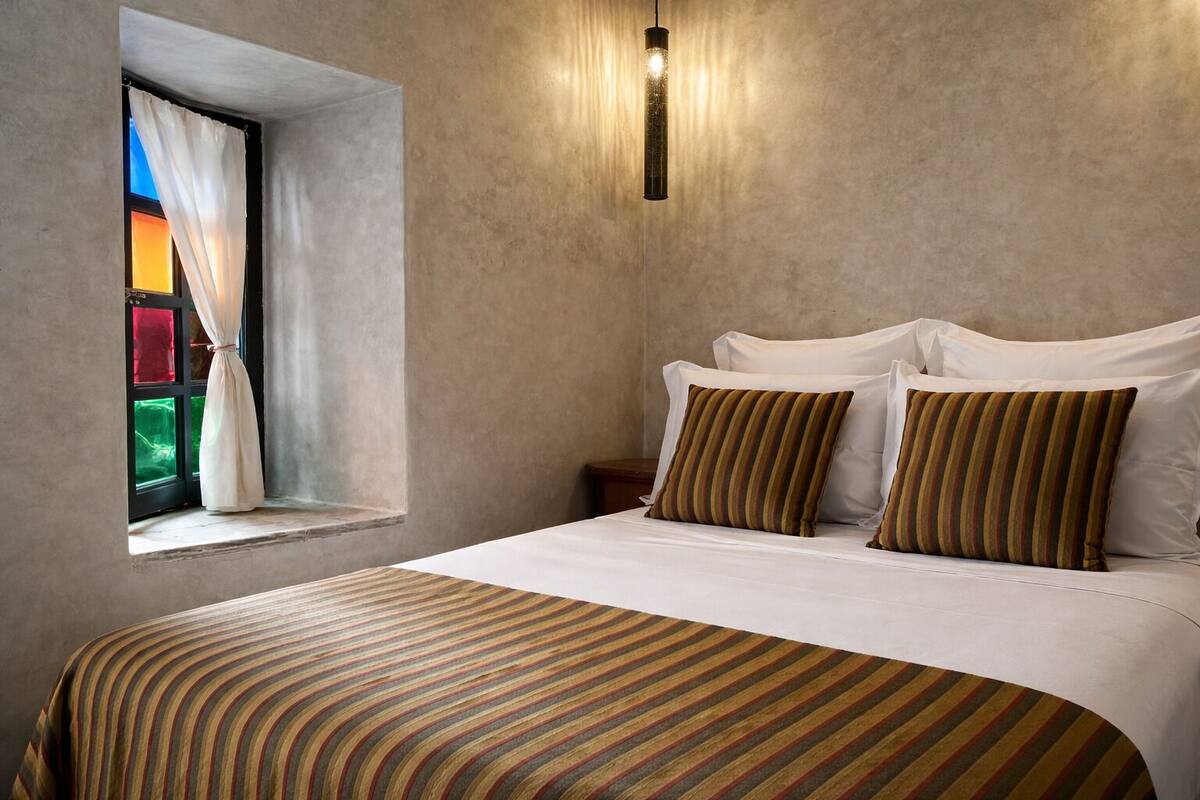 A bedroom with a bed, striped bedding, a window with curtains, and a wall-mounted light fixture.