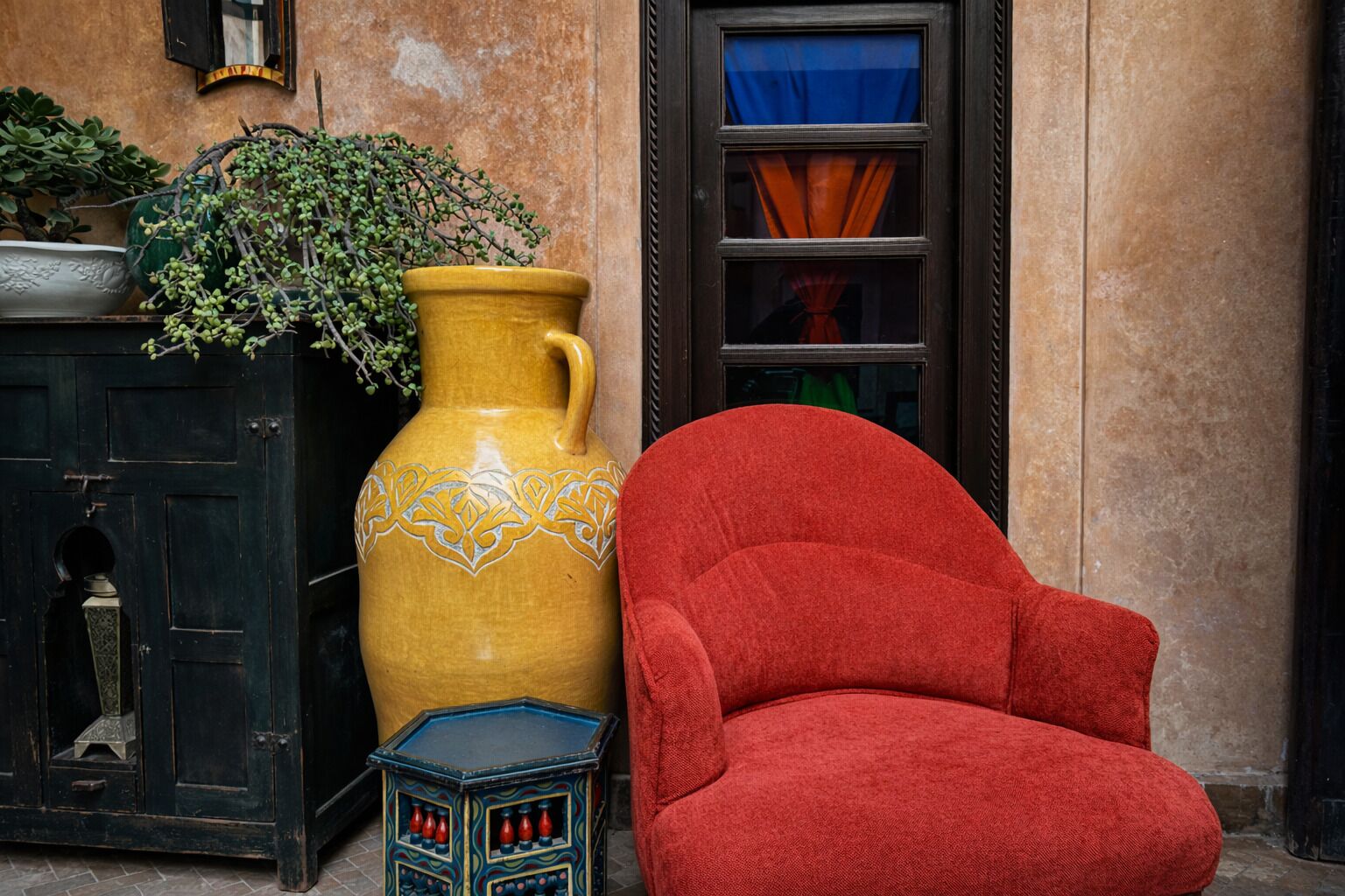A large yellow vase with a plant, a red armchair, and a small blue table with bottles.