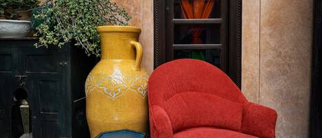 A large yellow vase with a plant, a red armchair, and a small blue table with bottles.