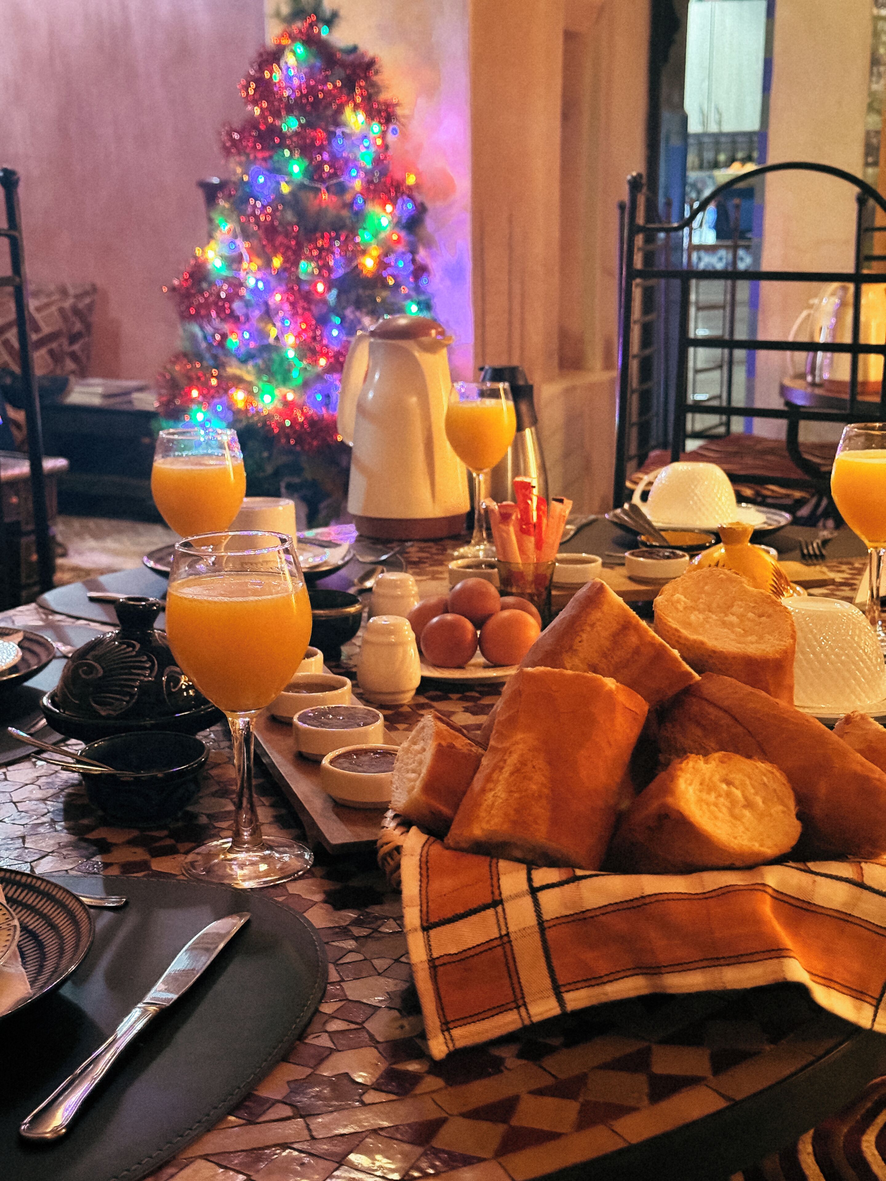 A breakfast setting with a Christmas tree, orange juice, bread, and a coffee pot.