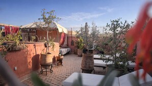 Un patio al aire libre con muros de terracota, plantas en macetas y una zona de estar cubierta.