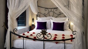 Una cama con dosel, ropa de cama blanca y flores rojas.