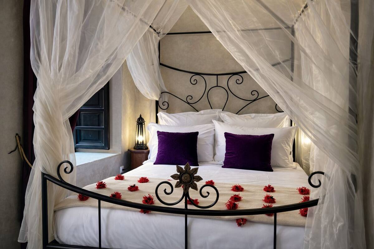 A bed with a canopy, white bedding, and red flowers.