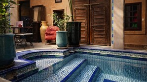 Un área de piscina con baldosas azules y blancas estampadas, una silla roja y jarrones grandes.
