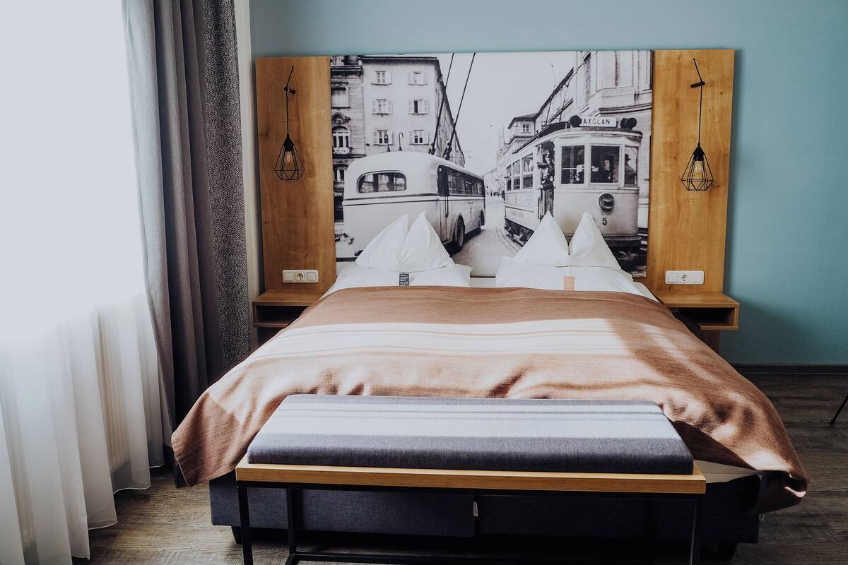 Un lit avec une tête de lit en bois, des oreillers blancs et une couverture marron.