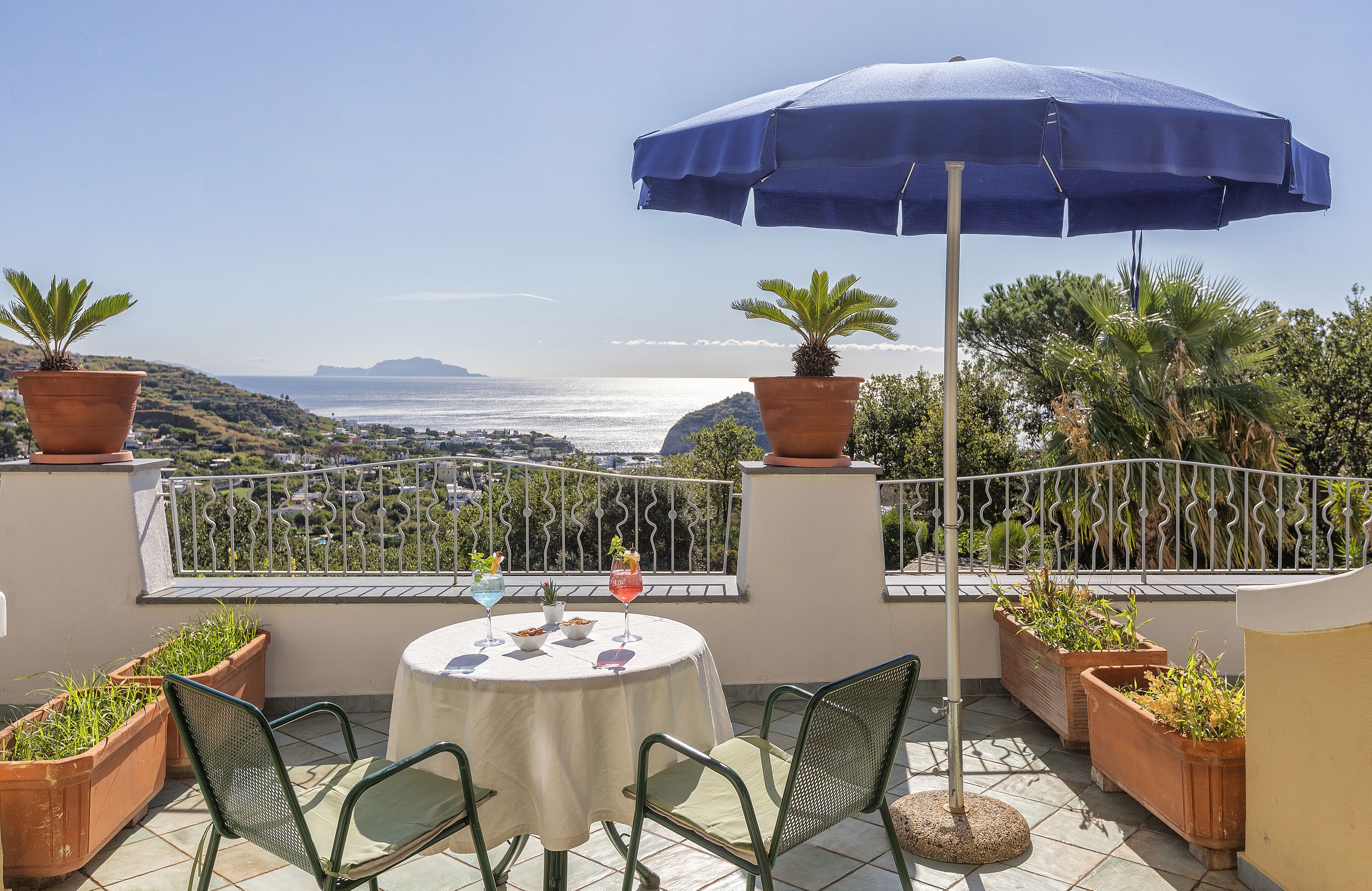 Eine Terrasse mit Tisch, Stühlen, Kübelpflanzen und Blick aufs Meer.
