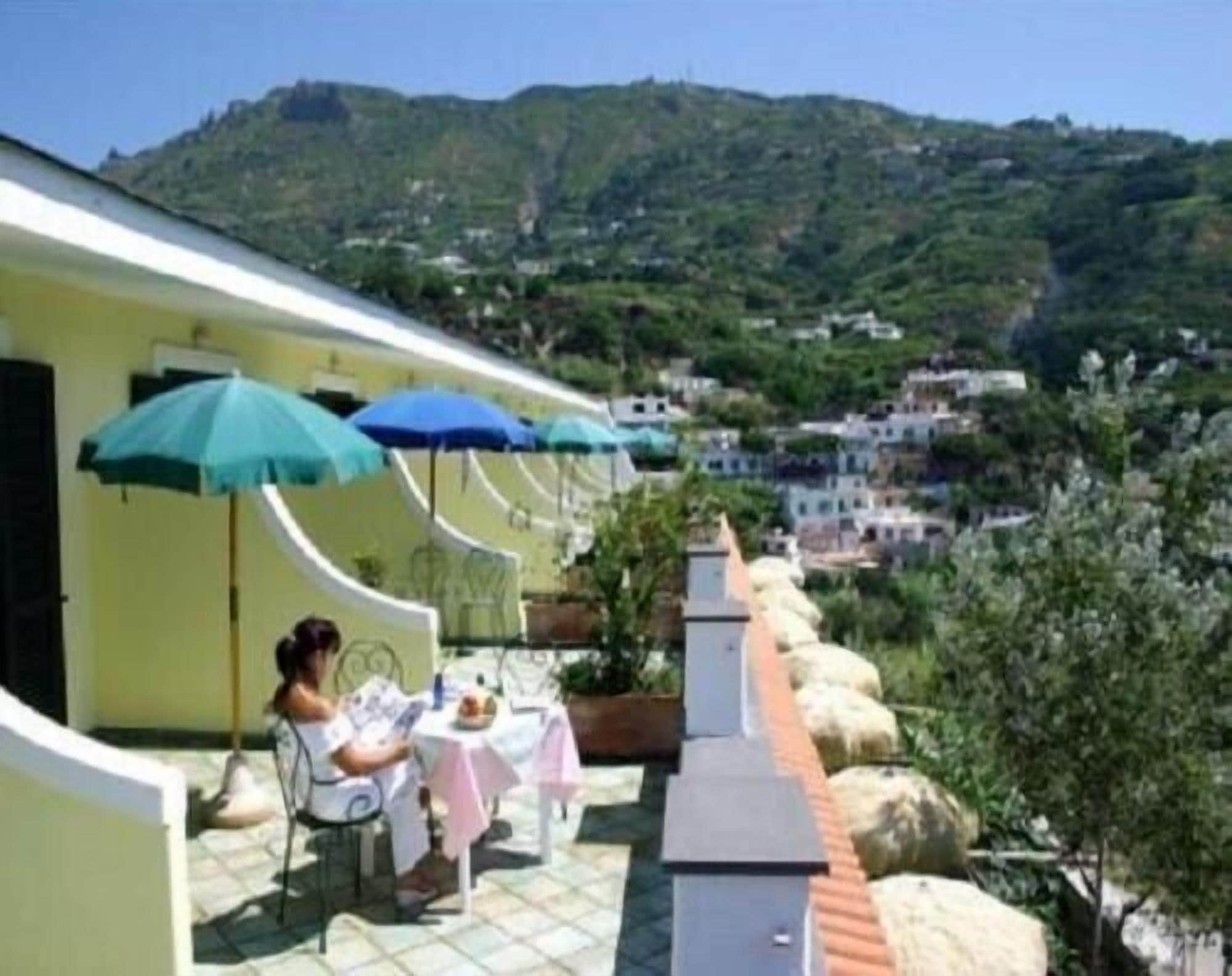 Una terraza con mesa y sillas, sombrillas y vistas a una colina con edificios.