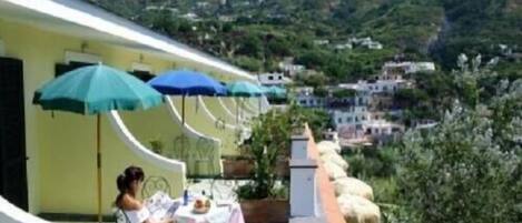 Una terraza con mesa y sillas, sombrillas y vistas a una colina con edificios.