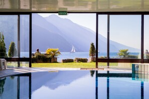 Ein Pool mit Blick auf ein Segelboot auf dem Wasser, umgeben von Grünpflanzen und Bergen.