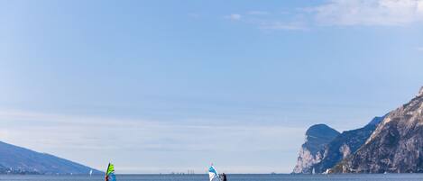 Two windsurfers on a calm sea with a mountainous coastline in the background.