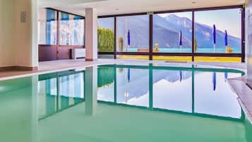 A modern indoor swimming pool with a clear view of a mountain and lake through large windows.