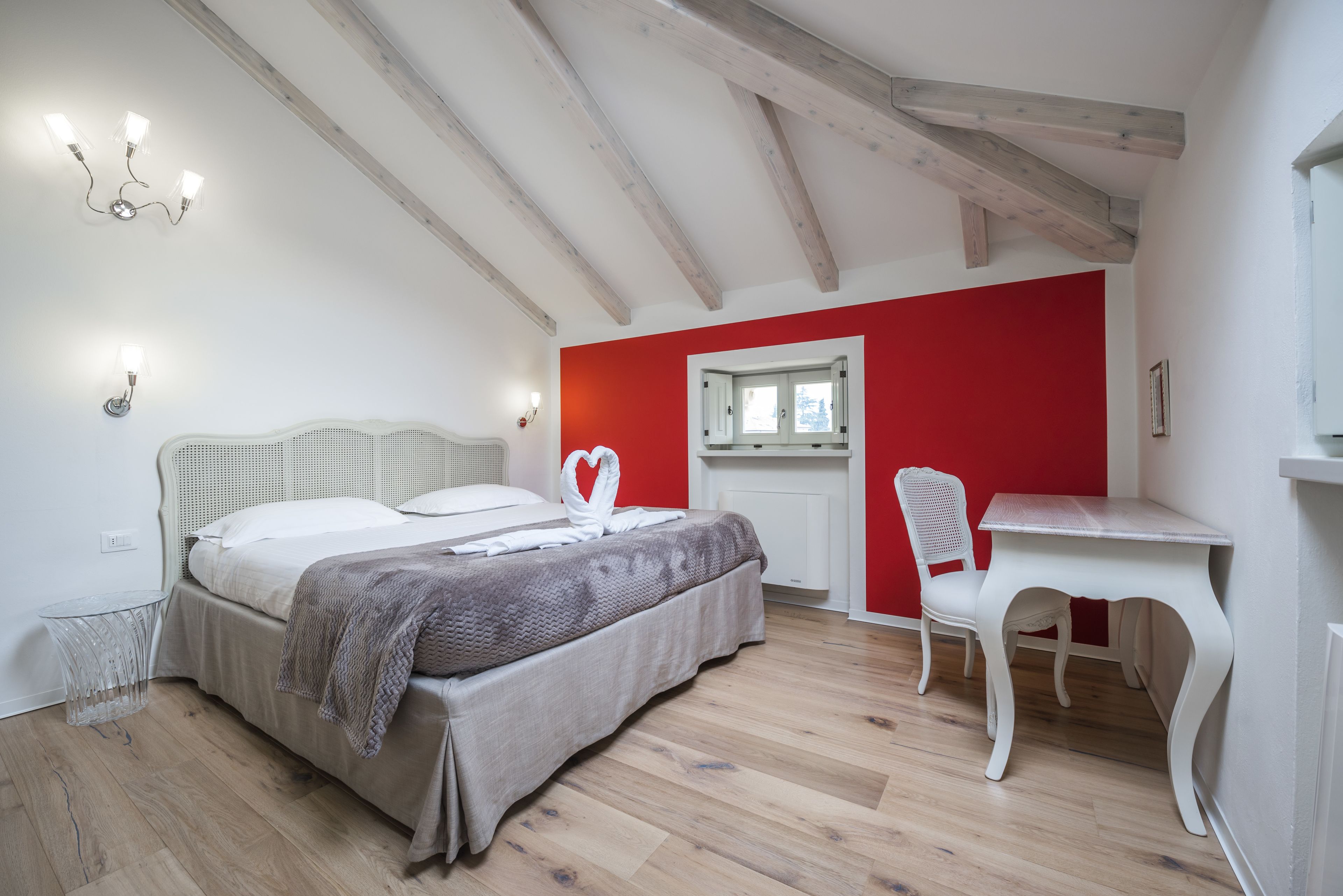 A bedroom with a bed, a desk, a chair, and a red accent wall.