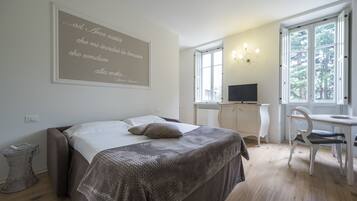 Een slaapkamer met een bed, een bureau, een stoel en een groot raam.