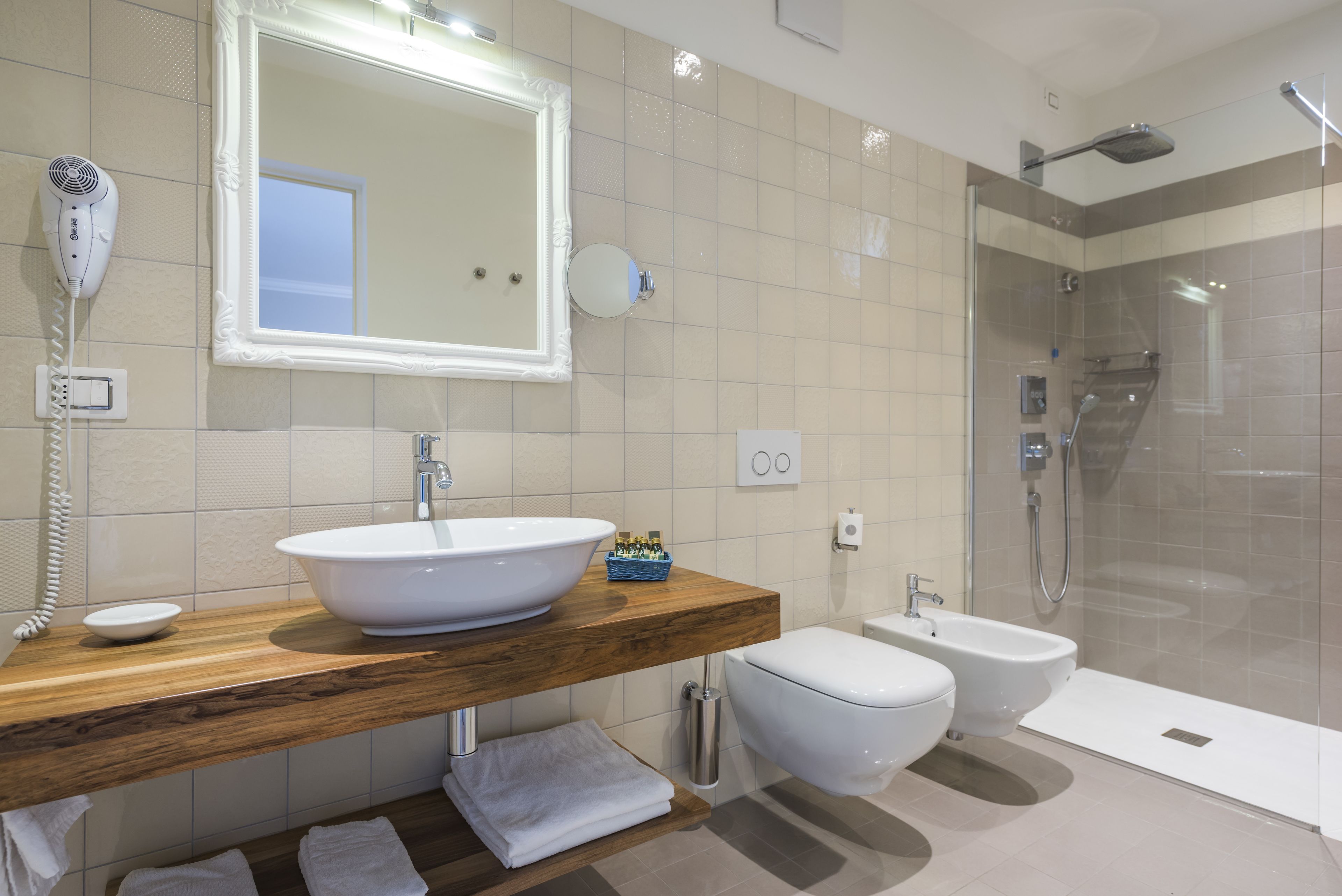 A modern bathroom with a wooden vanity, a large mirror, a white sink, a toilet, a bidet, and a glass-enclosed shower area.